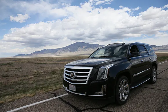 A black Cadillac Escalade in front of a mountain on a cloudy day.
