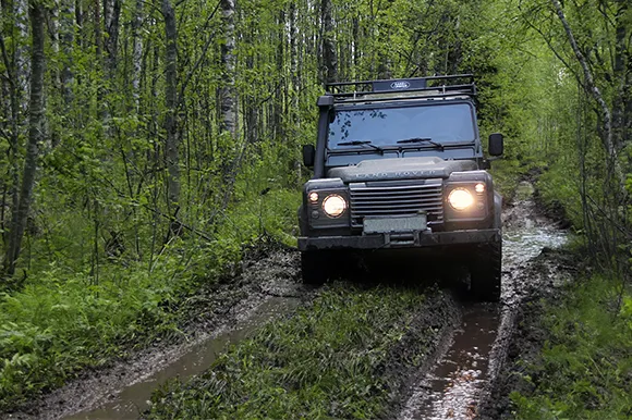 A black Land Rover Defender driving through a muddy forest.