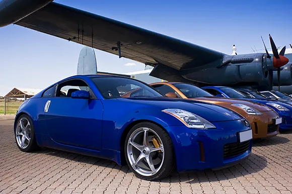 A blue Nissan 350Z and other different colored Nissan 350Z underneath the wing of a plane.