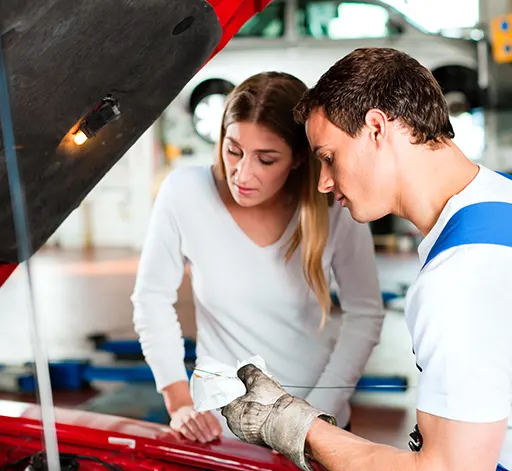 A mechanic and a young woman looking under the hood of a car