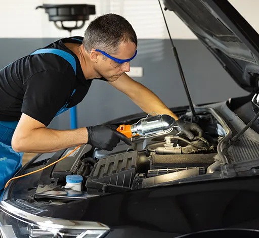 An auto mechanic using a work light to inspect a car's engine