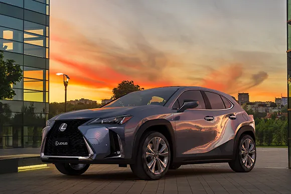 A grey Lexus UX parked between two modern office buildings.