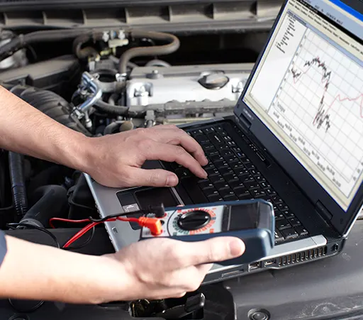 A car mechanic using a laptop and a digital multimeter to perform an auto repair service