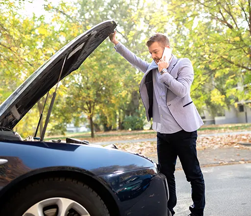 A young businessman checking under the hood of his car