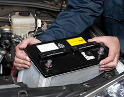 An auto mechanic carefully removing and replacing a car battery