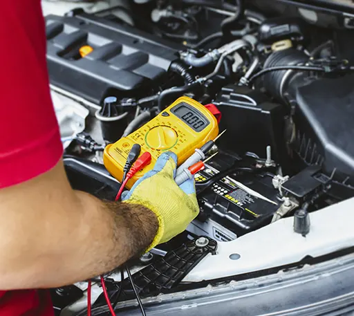 A professional mechanic using a yellow digital multimeter to measure a car's electrical values