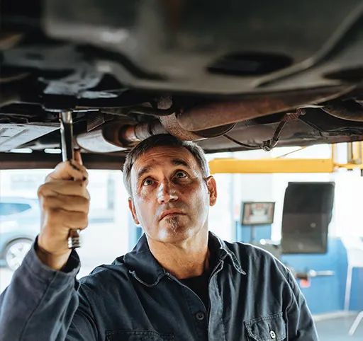 An auto mechanic repairing the exhaust system of a lifted car