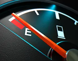 A car's gas gauge with the needle indicates a nearly empty tank