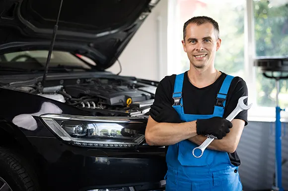A professional auto mechanic with a spanner posing in front of a car with its hood open
