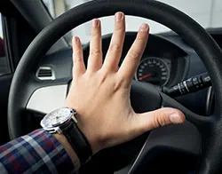 A driver's hand pressing firmly against the car horn switch